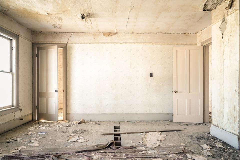 Pièce vidée de ses revêtements : murs à nu, débris au sol, portes encore en place